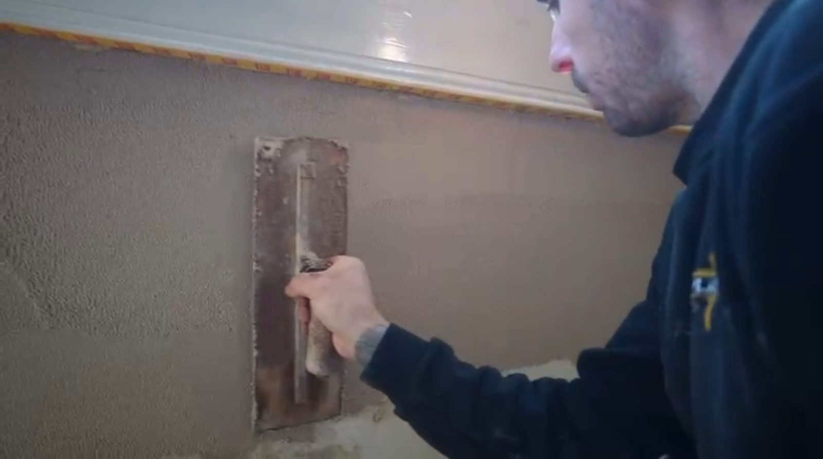 Close-up of a trowel flattening a skim coat on a wall