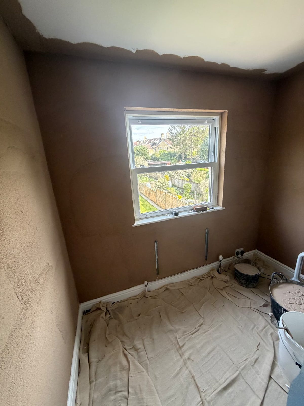 Bedroom walls in backing plaster around a sash window, floors covered with dust sheets