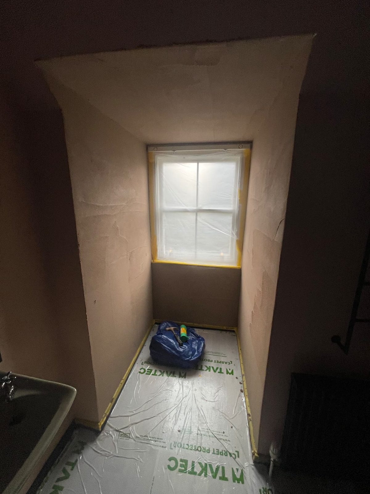 Freshly plastered window reveal with the floor sheeted and the window masked up