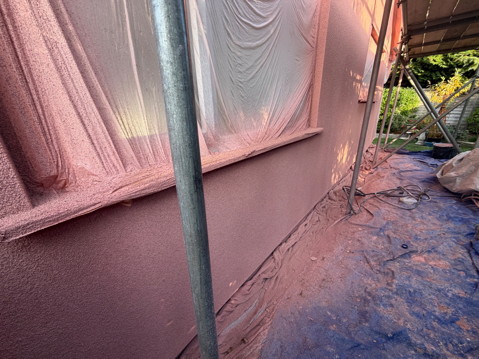 Work in progress in Frome: window masked with protective sheeting while the blush pink spray cork coating is applied to the wall