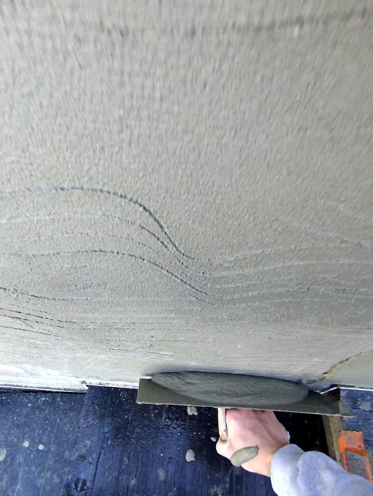 Grey lime plaster being trowelled across a ceiling